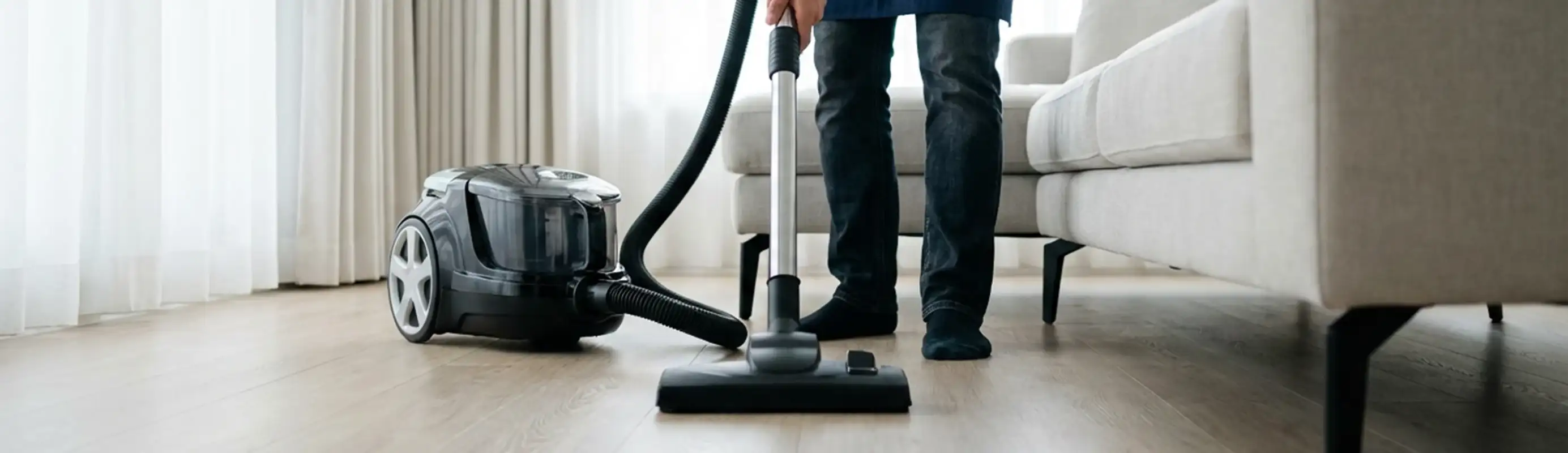 Professional house cleaner vacuuming a living room floor with a canister vacuum cleaner, Pasadena, CA.