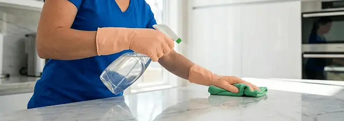 Maid service worker spraying and wiping a kitchen countertop with a microfiber cloth for sanitizing, Pasadena, CA.