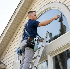 Professional window cleaner on a ladder using a squeegee to clean an exterior arched window, Pasadena, CA.