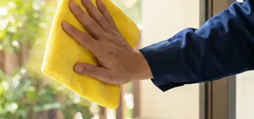 House cleaner wiping a glass window with a yellow microfiber cloth for streak-free cleaning, Pasadena, CA.